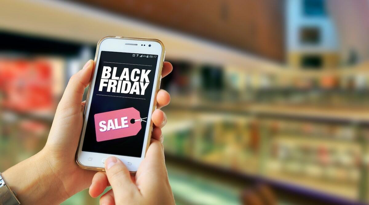 Smartphone displaying Black Friday sale sign in a bustling shopping environment.