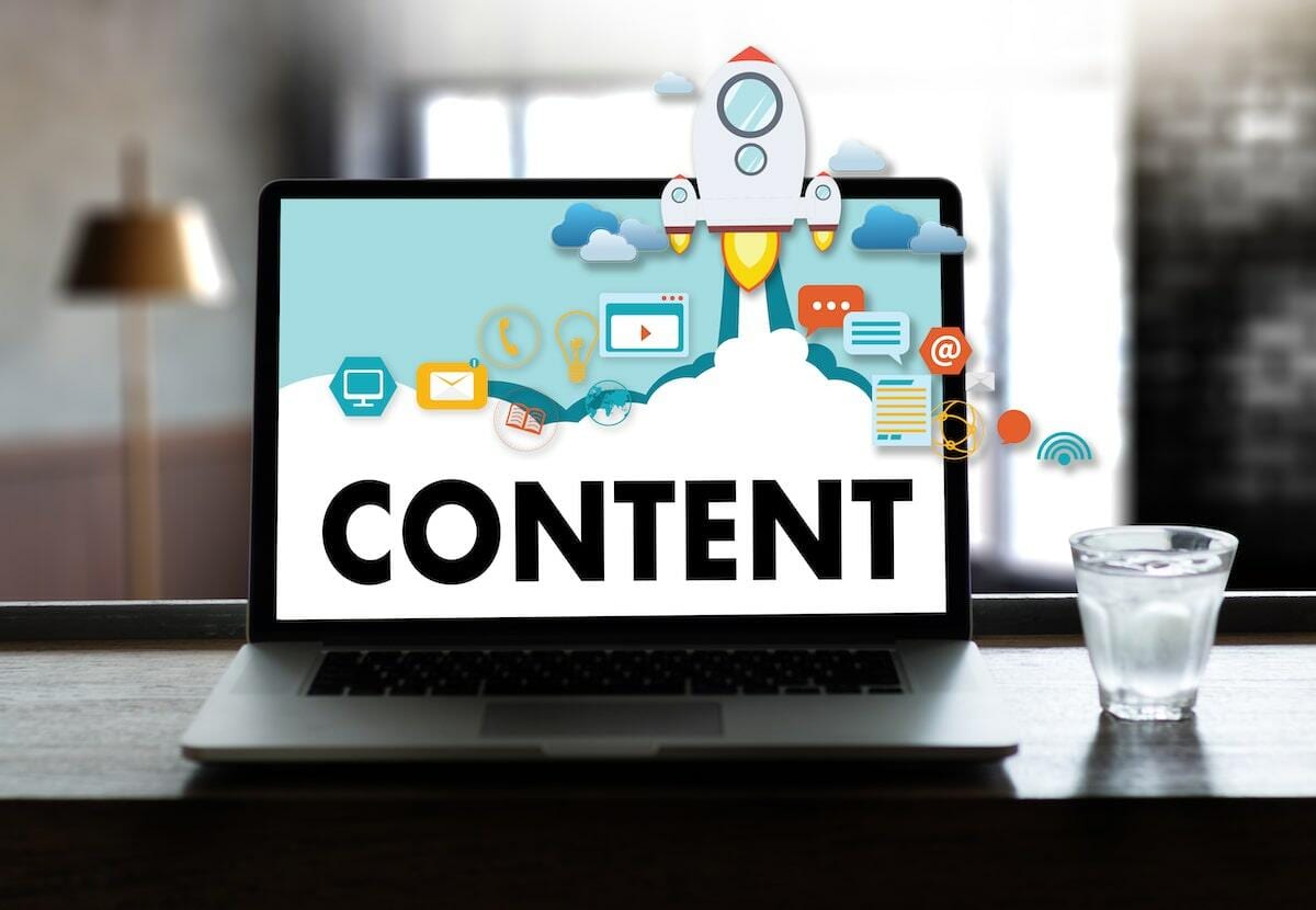 Laptop displaying the word 'Content' with digital marketing icons and a rocket, glass of water on the side.