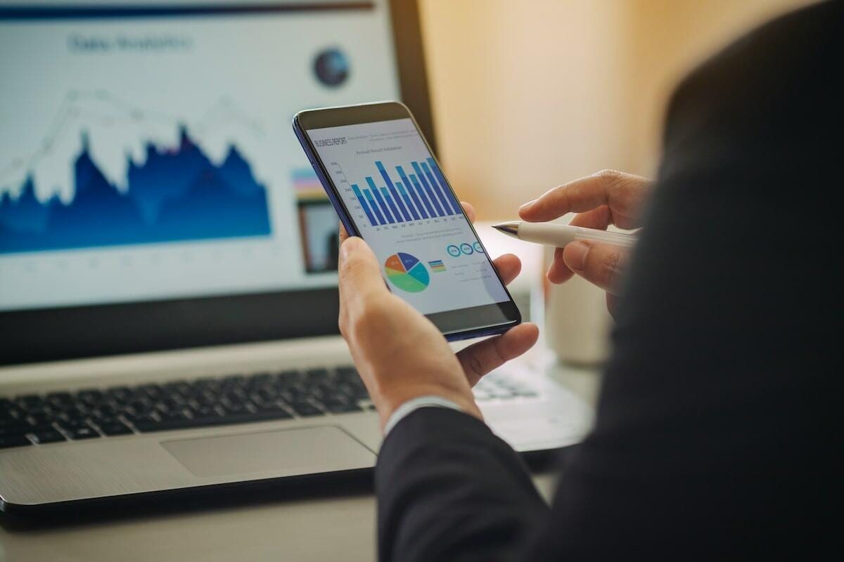 Business professional analyzing graphs on smartphone and laptop