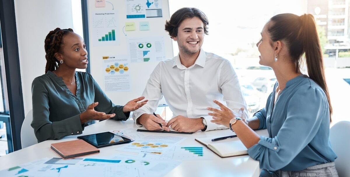 A diverse team discusses strategies at a meeting table, surrounded by charts and graphs.