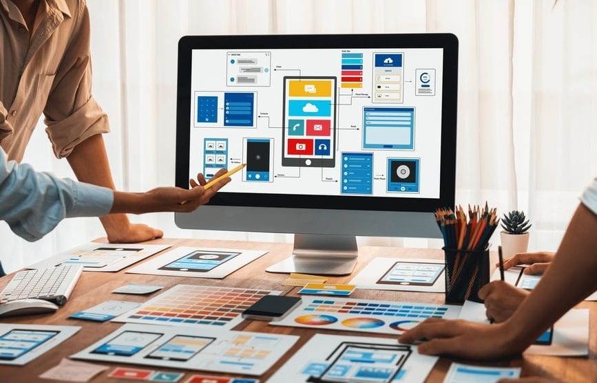Team collaborating on web design with graphics and wireframes displayed on a computer screen.