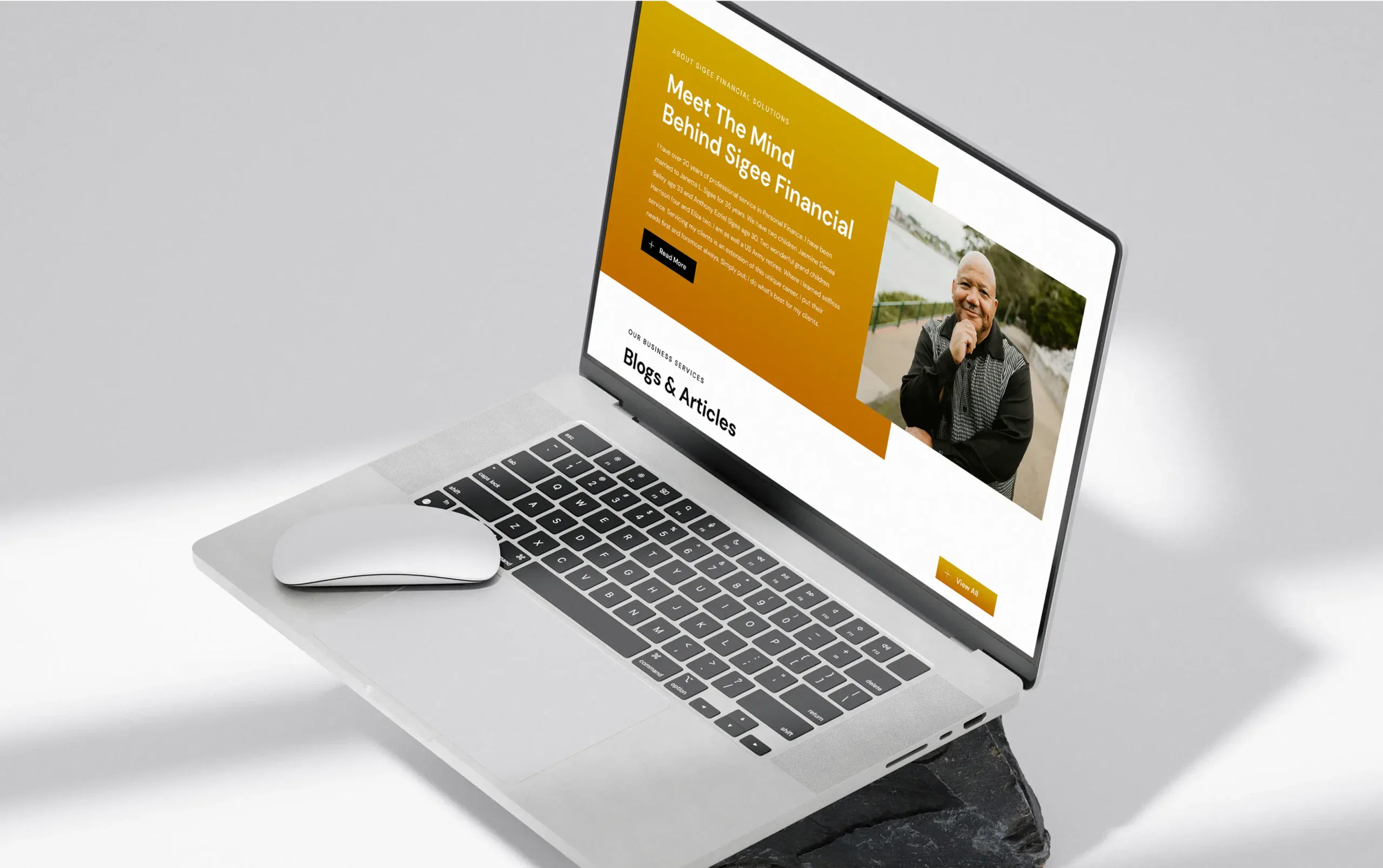 Open laptop displaying a website profile of a smiling individual, with a white wireless mouse beside it.