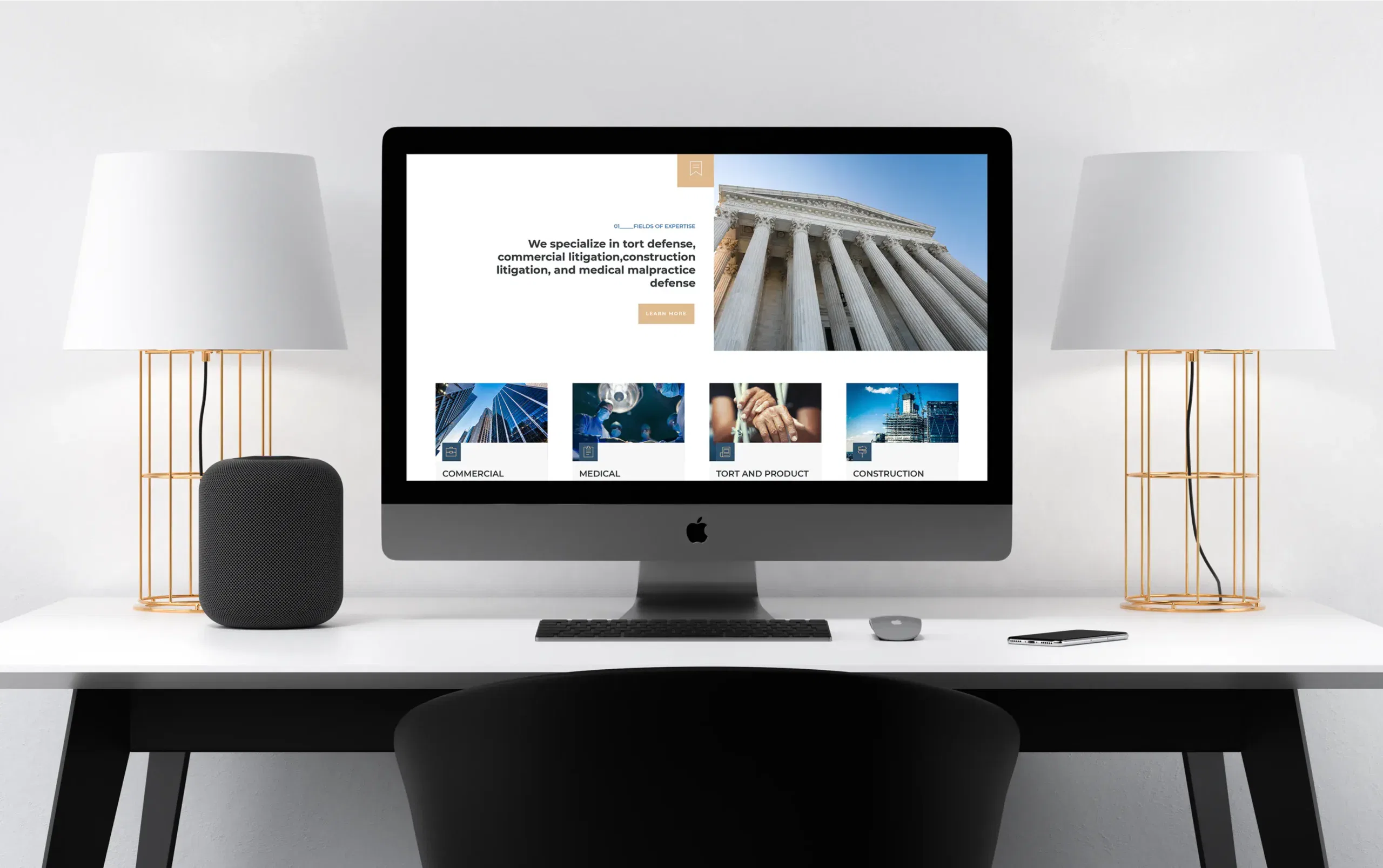 Modern computer desk setup with iMac displaying a professional website, flanked by elegant lamps.