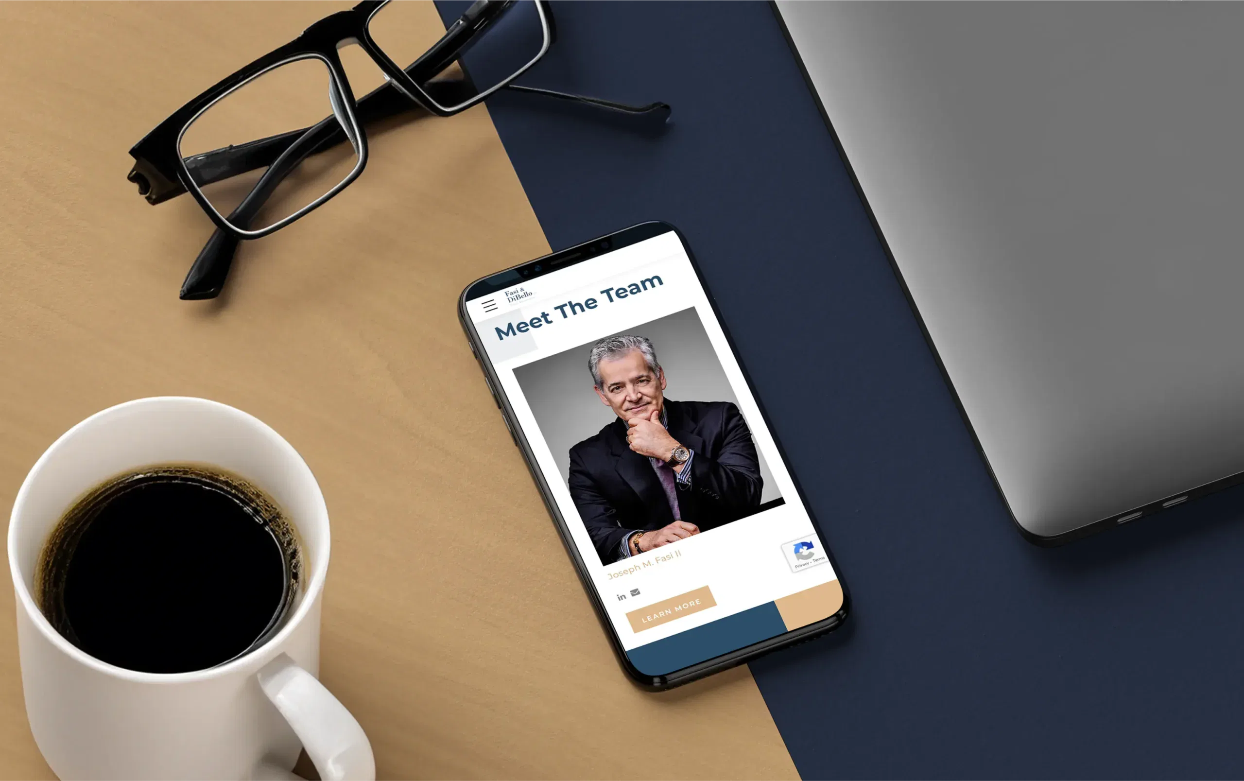 Smartphone on desk displaying a smiling man, with a coffee cup, glasses, and laptop nearby.