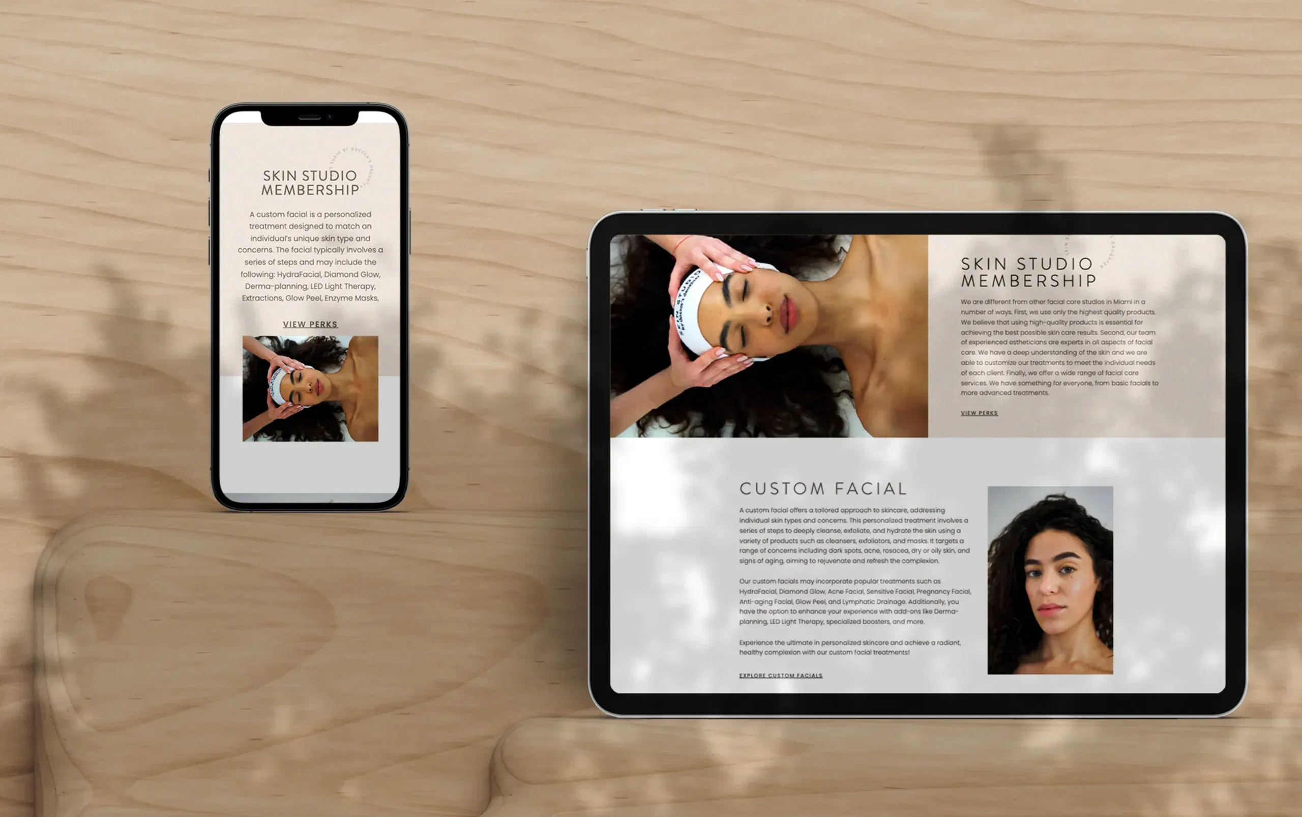 Mobile phone and tablet displaying a website about custom facial treatments on a wooden surface.