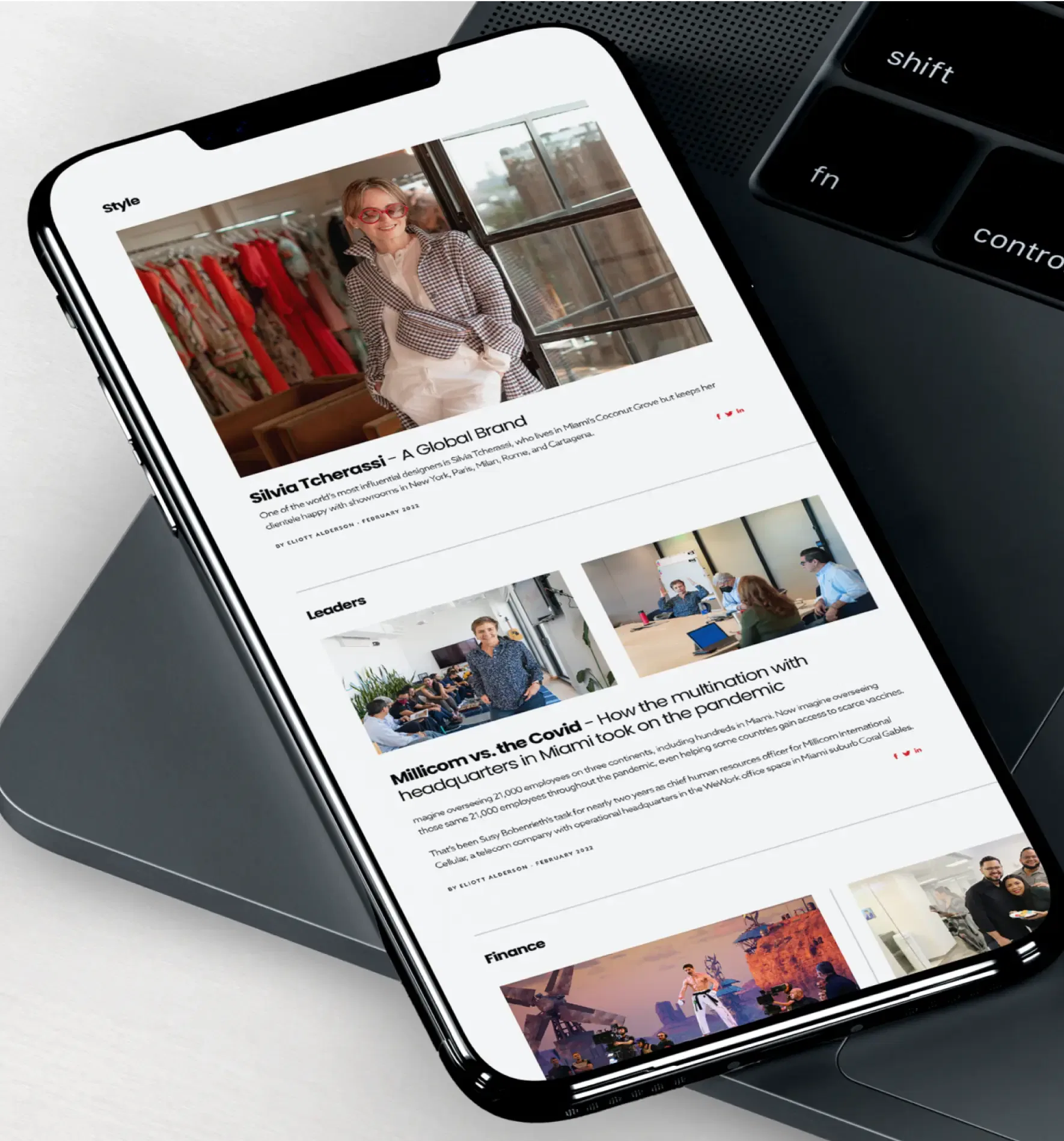 Smartphone displaying a news app interface with articles and a laptop keyboard beside it.
