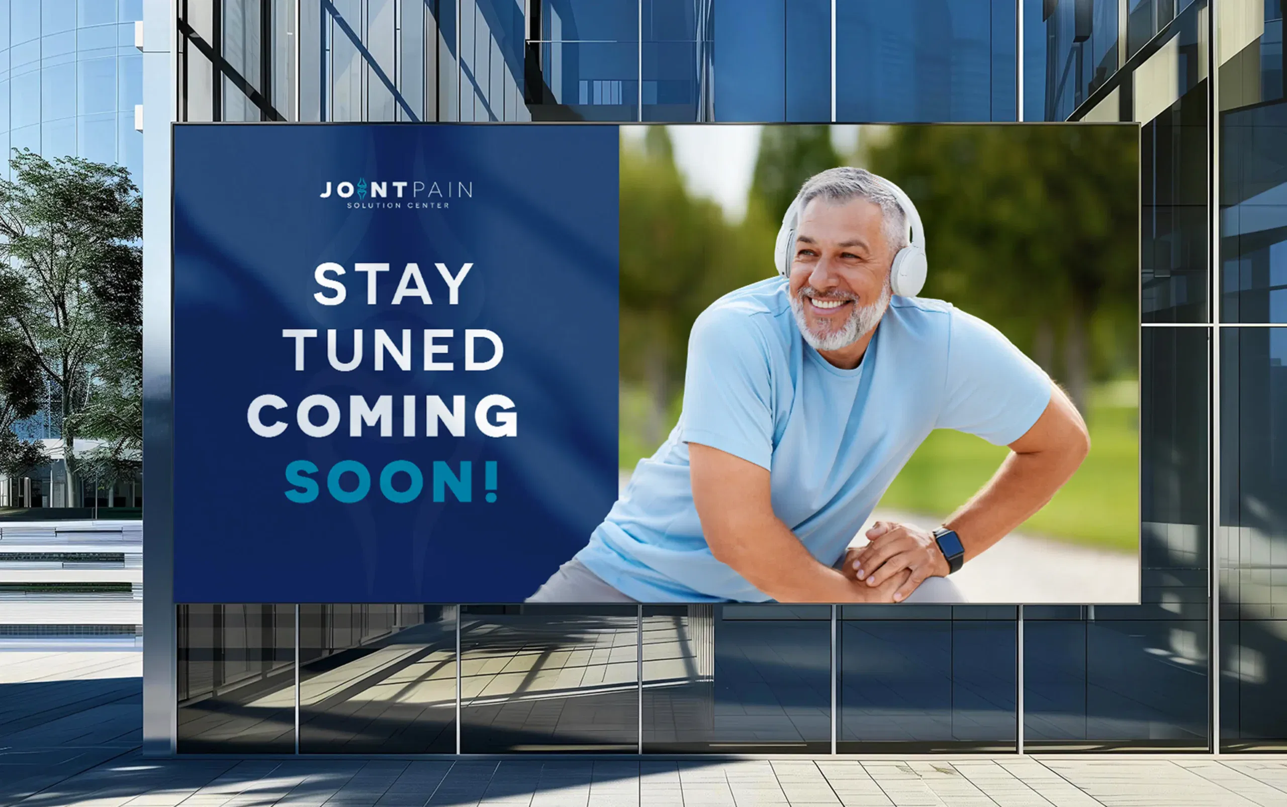Smiling man wearing headphones in a promotional billboard outside a modern glass building.
