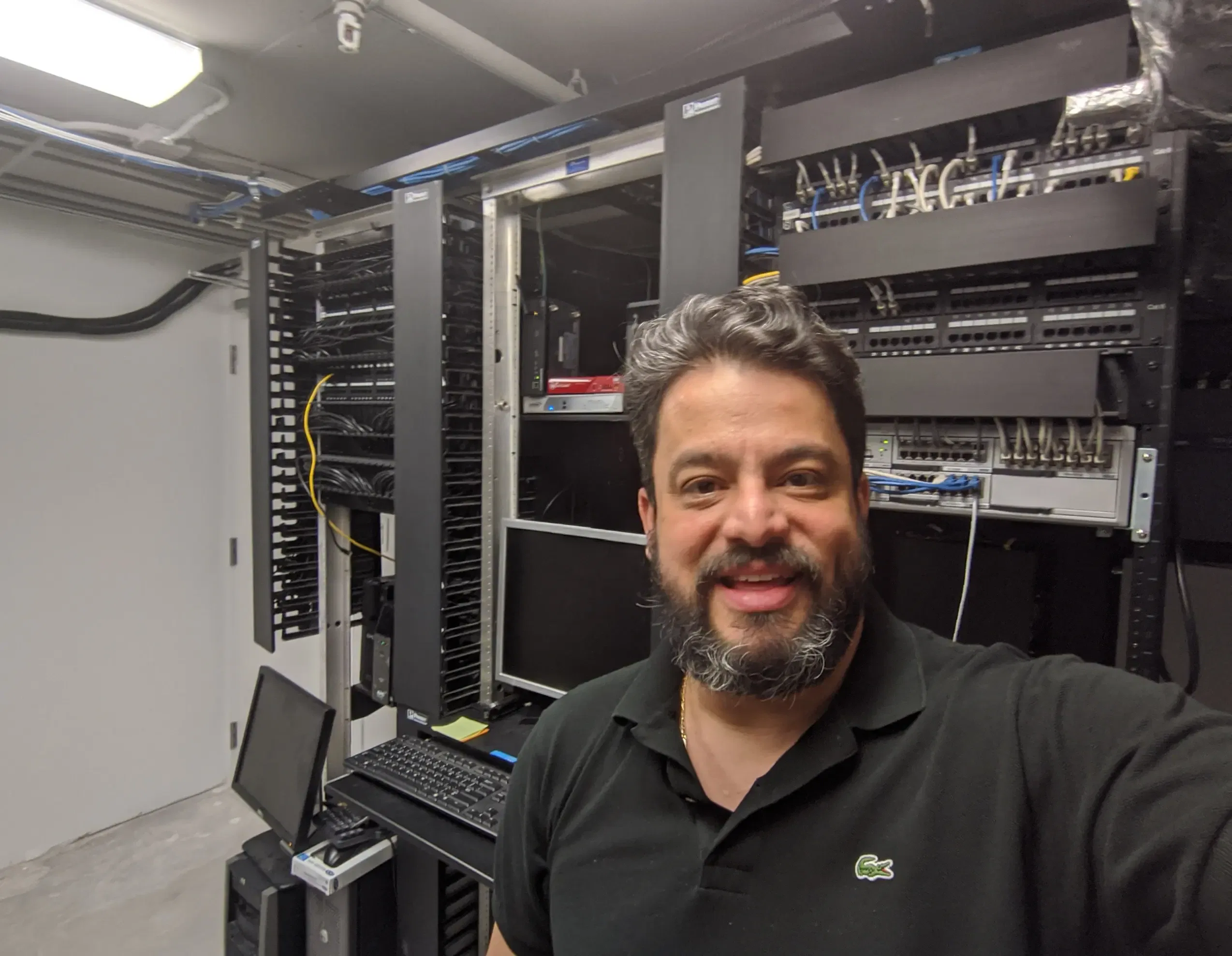A man smiling in a server room with visible racks and cables.