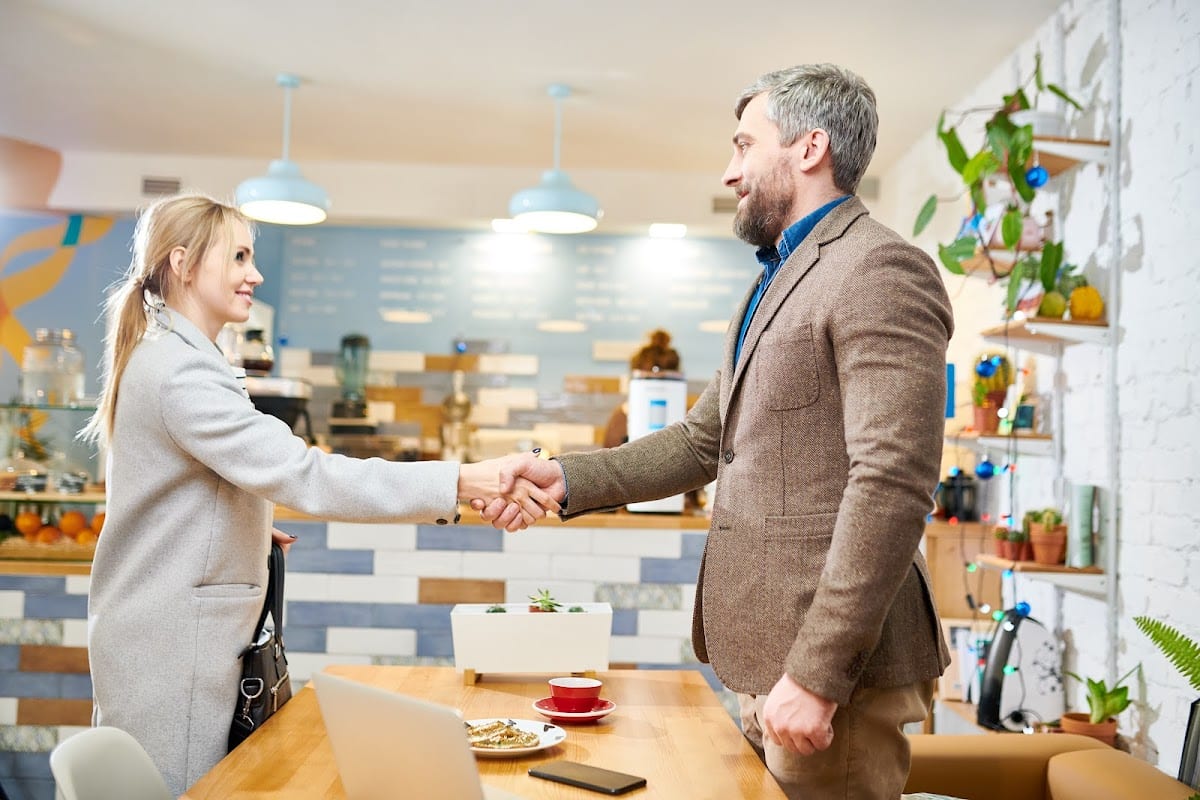 Business professionals shake hands in a modern cafe, sealing a deal with smiles.