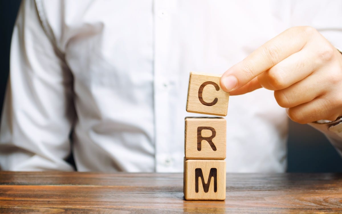 Hand stacking wooden blocks spelling CRM on a wooden table.