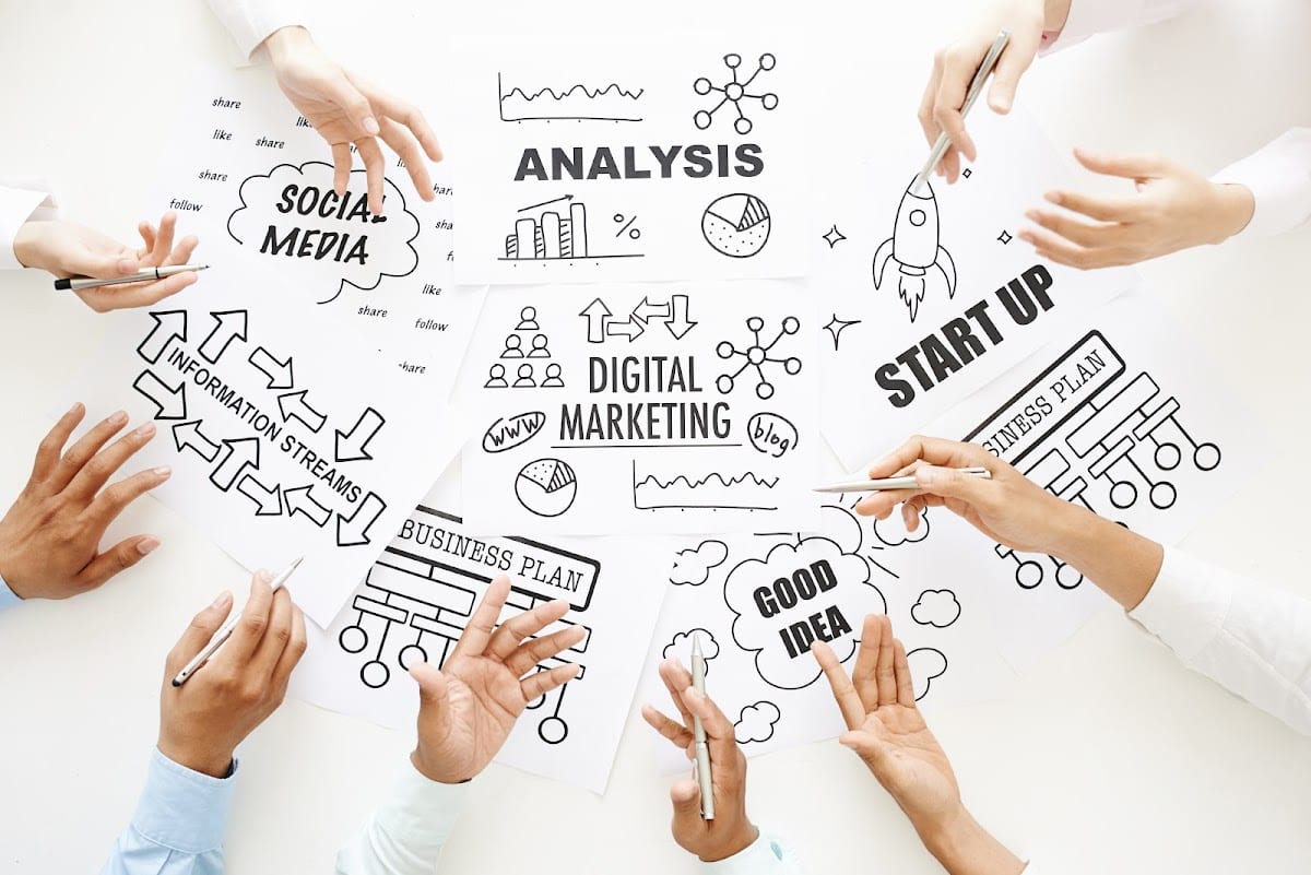 Diverse group collaborating on a digital marketing brainstorming session with charts and strategy sketches.