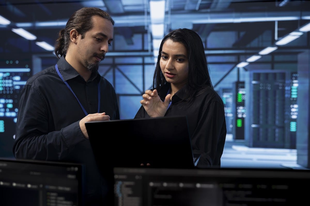 Two coworkers collaborate in a modern server hub workspace, working on fixing technical issues together.