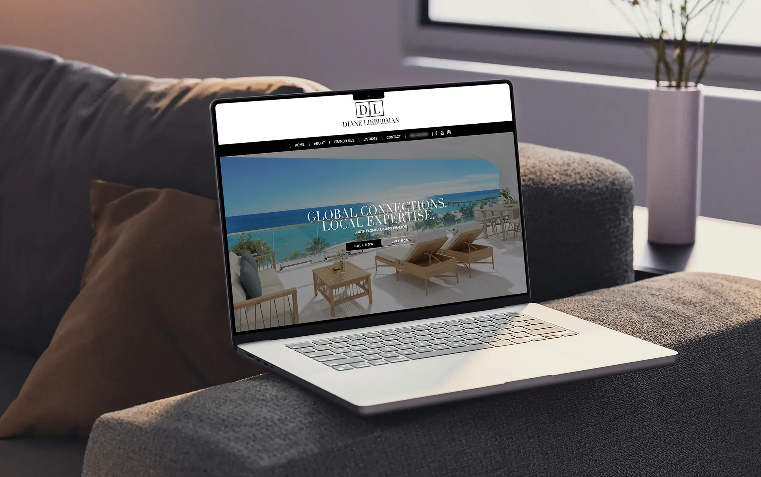 Laptop displaying a luxury real estate website on a cozy couch in a well-lit room.