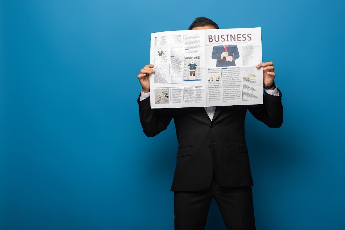 Businessman in suit holding a newspaper on a blue background.
