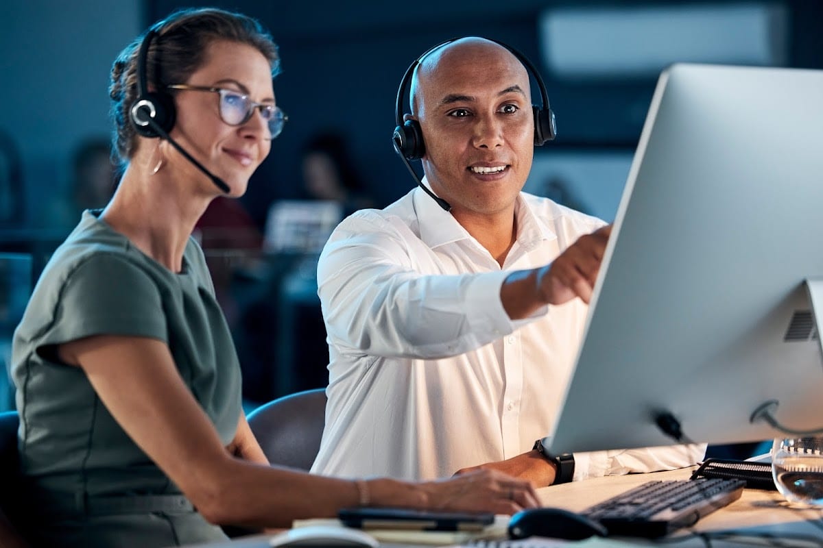 Colleagues in a modern office using computers and headsets for online training.