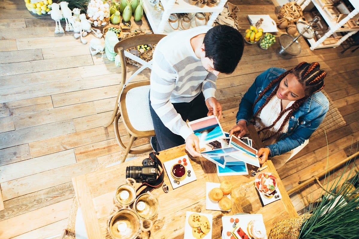 Two people selecting photos at a rustic table with snacks and camera gear.