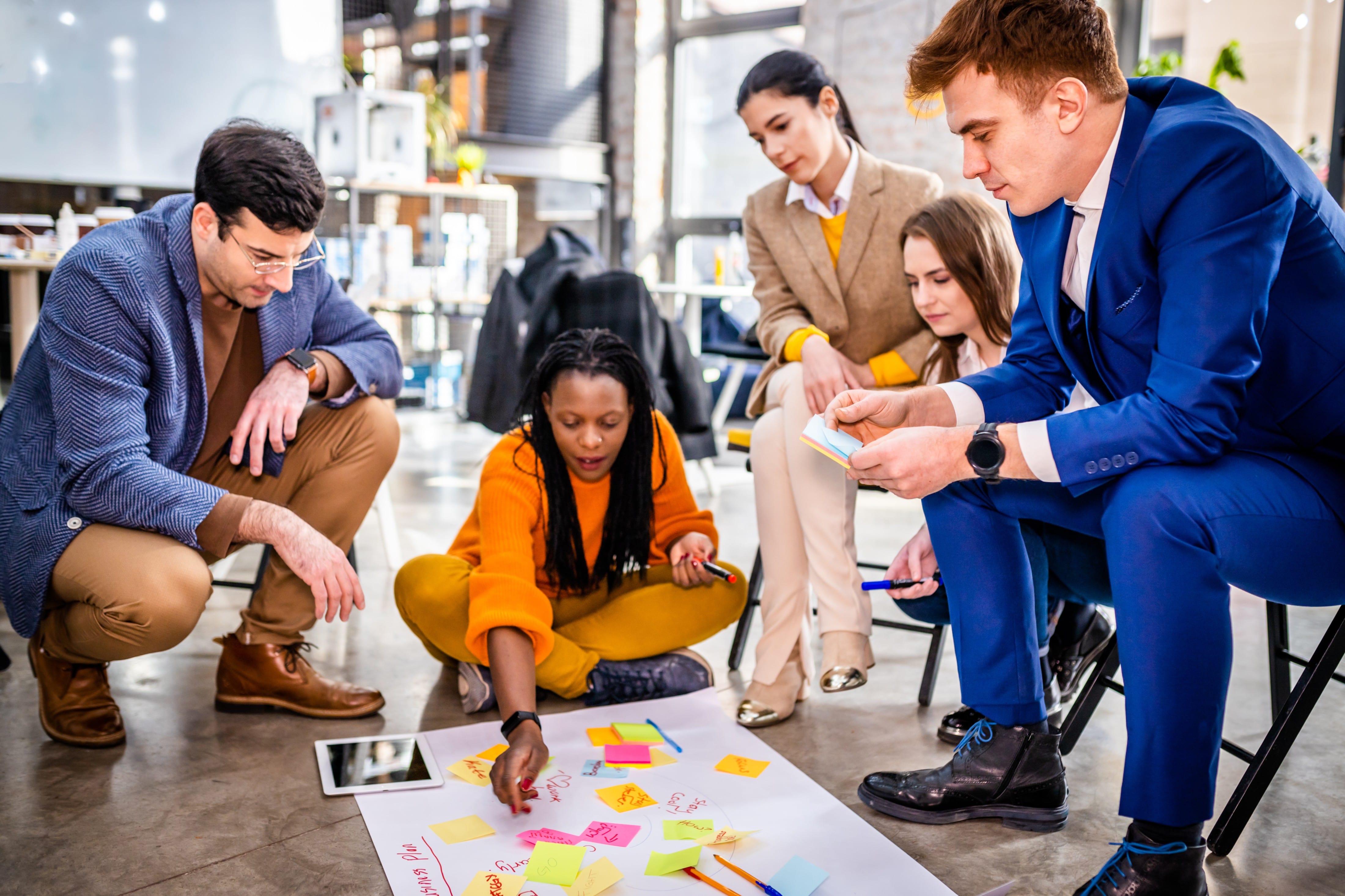 Group brainstorming session with diverse team using sticky notes on the floor in a trendy office space.