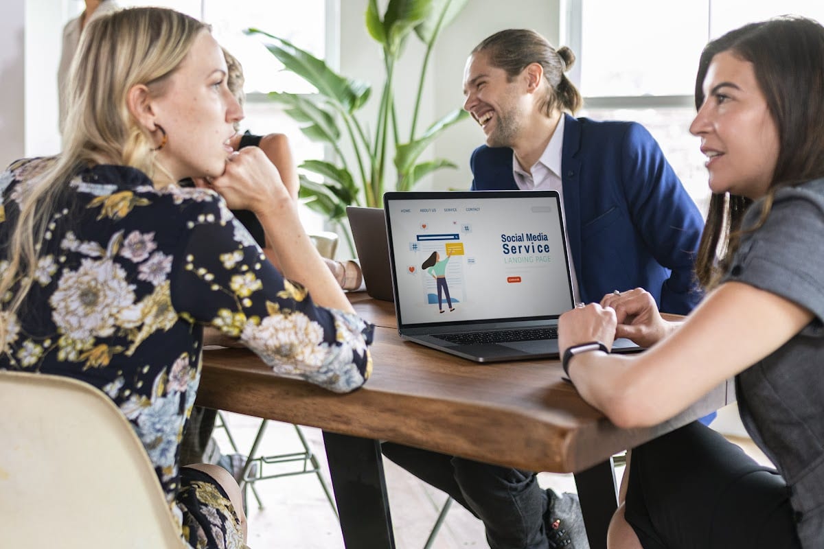 Group of colleagues engaged in a creative meeting around a laptop displaying social media services.